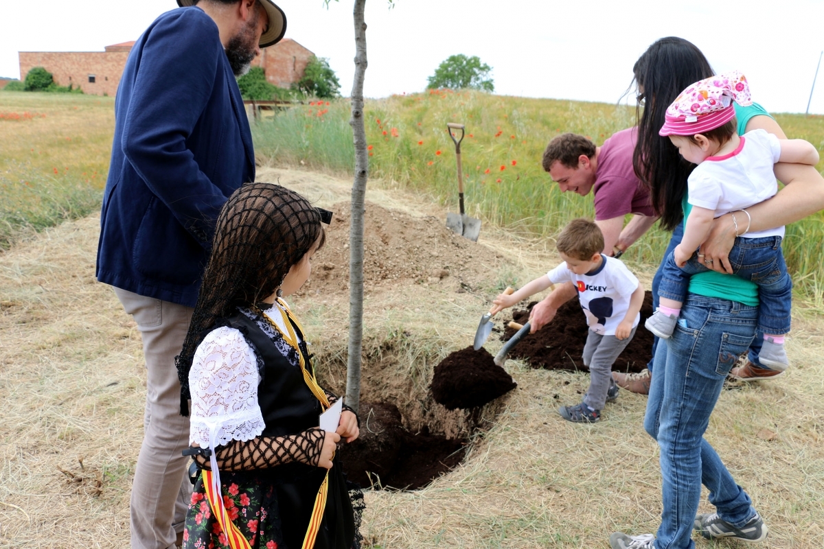 Una de les famílies, en el moment de plantar l'arbre davant la mirada de l'alcalde, a l'esquerra