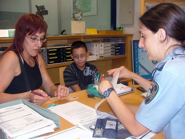 Gemma Serrano, observada pel seu fill, omple els formularis per dipositar les claus davant una agent de la Policia Municipal de Sallent / Foto: Marc Riera, ACN